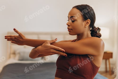 Preview: Smiling young African American woman stretching her hand before training while standing at home