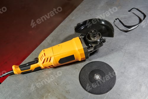 Preview: yellow beautiful angle grinder, cutting disc and goggles lie side by side on a metal workbench table