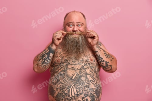 Preview: Funny bearded man touches mustache, stands naked with big belly, tattooed body, has fun and talks wi