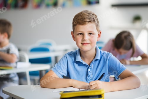 Um pequeno estudante sentado à mesa da sala de aula na aula, olhando para a câmera