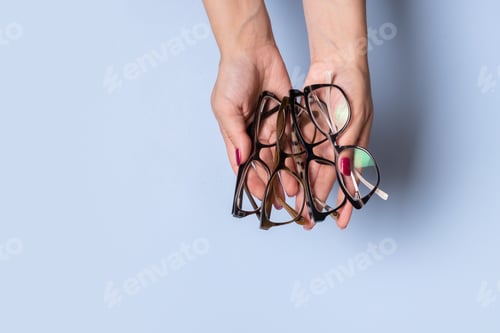 Preview: Female hands with eye glasses on blue background. Optical store concept