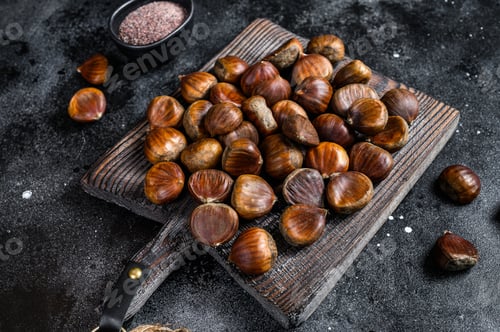 Preview: Raw chestnuts on a wooden cutting board. Black background. Top view