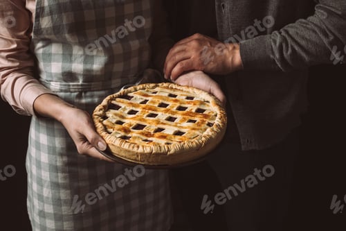 Preview: cropped shot of woman holding homemade pie with husband near by