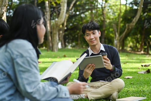 Preview: Smiling young asian male checking university schedule on digital tablet and talking with his friend.