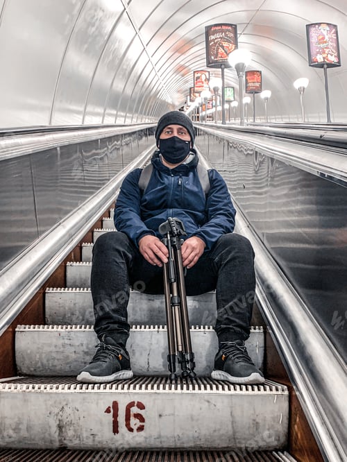 Preview: A masked man is sitting on the steps of an escalator in the subway