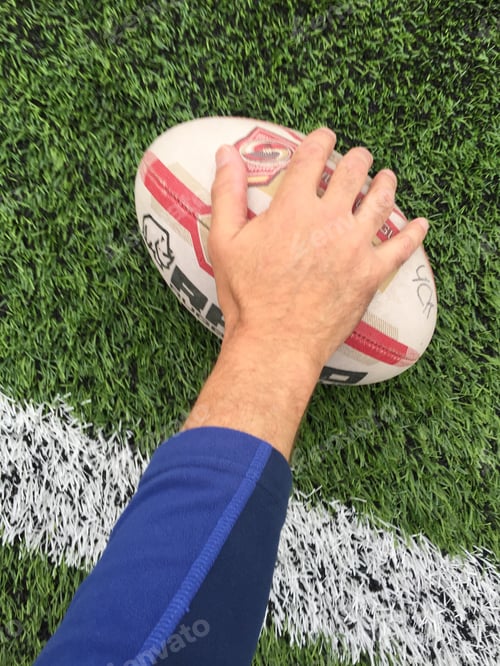 Preview: A rugby player’s hand and arm reaching over the try line to touch the ball down for a score on grass