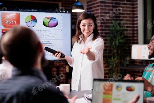 Preview: Smiling business employee standing in front of tv screen with sales statistics talking with man with