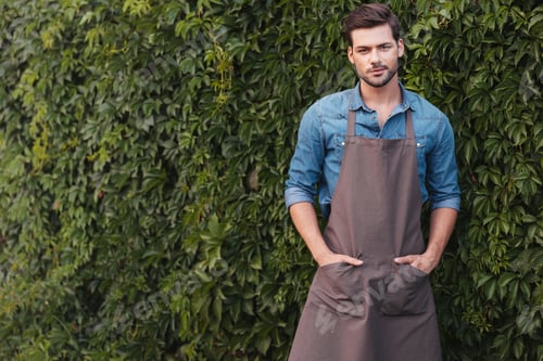 Preview: portrait of thoughtful gardener in apron looking at camera while standing in garden