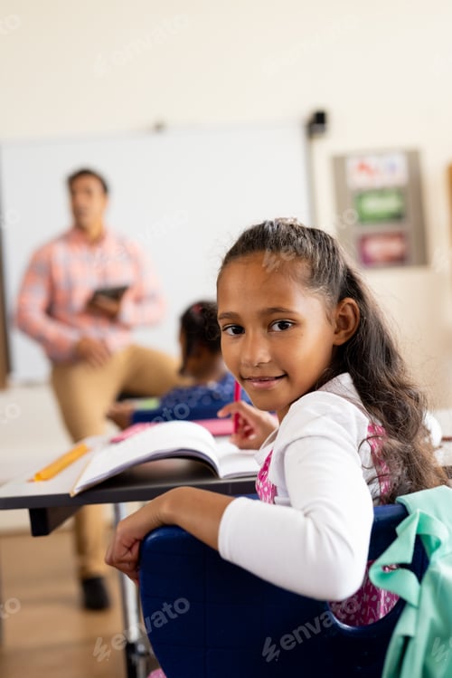 Visualização: Retrato de feliz aluna birracial do ensino fundamental sentada à mesa na sala de aula