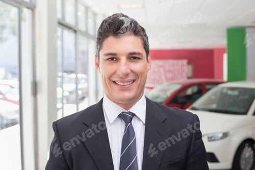 Preview: Middle-aged man wearing suit and striped tie standing by display cars in showroom by glass windows