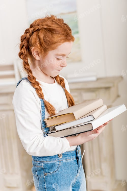 Preview: Portrait of adorable little redhead girl holding pile of books at home