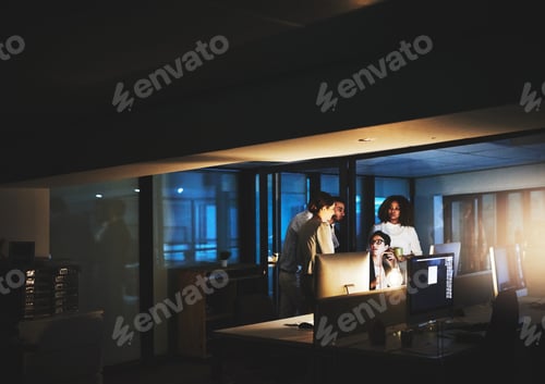 Preview: Shot of colleagues standing together as they work on something on a computer at night
