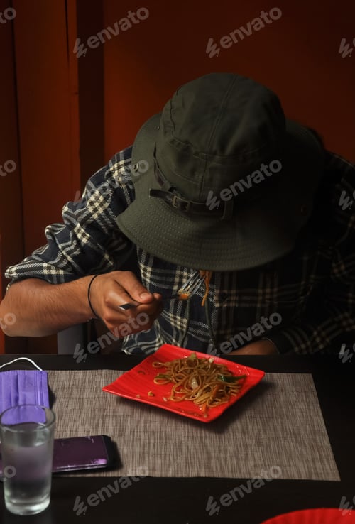 Preview: A man with wearing boonie hat eating noodles in the cafe during coronavirus pandemic