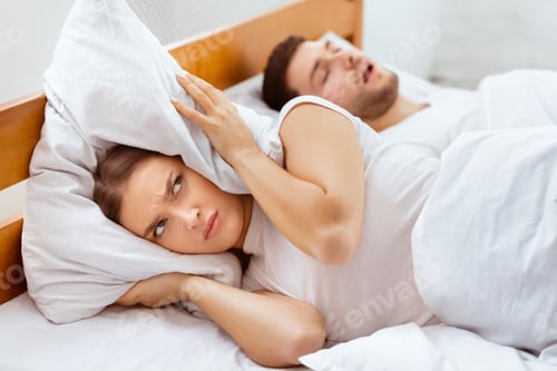 Preview: Woman Covering Ears Lying Near Snoring Husband In Bed Indoor