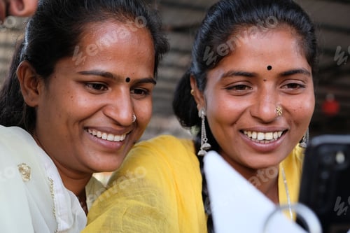 Preview: Smiling Indian female friends sitting in a cafe looking at the phone