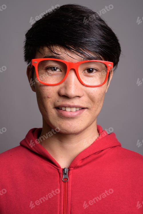 Preview: Young Asian man wearing red jacket with eyeglasses against gray
