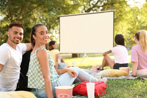 Preview: Young couple with popcorn watching movie in open air cinema. Space for text