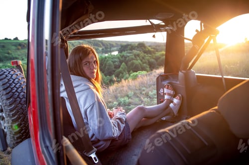 Preview: A young woman enjoys the sunset while sitting in the trunk of an SUV.