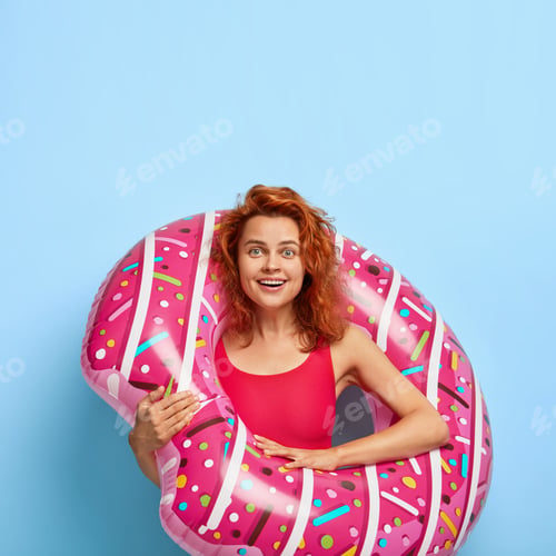 Preview: Photo of happy redhaired woman dressed in bikini, poses with swimring, enjoys summer vacation, isola