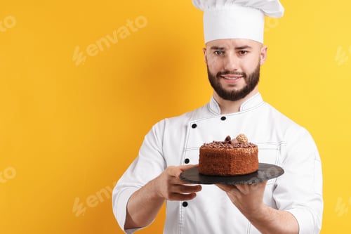 Preview: Happy confectioner in uniform holding chocolate cake on orange background