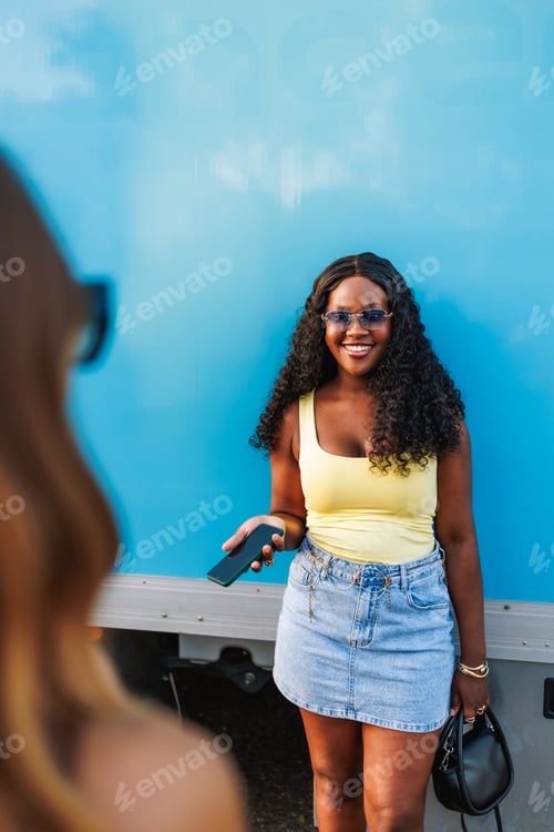 Preview: Young woman in casual clothes smiling and holding a smartphone against a blue background