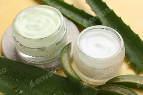 Preview: Moisturizing cream with extract of aloe vera and cut leaves on yellow background, closeup