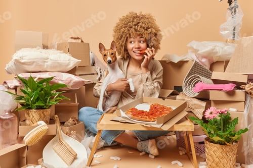 Preview: Photo of lovely young woman with curly hair eats appetizing pizza embraces pet dog sits on floor sur
