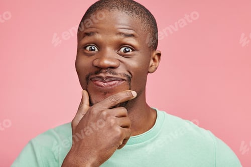 Preview: Joyful stylish dark skinned male keeps hand under chin, smiles gently, being happy or pleased to hea