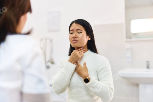 Preview: An Asian female patient has a sore throat and touching her neck, sitting with a female doctor.