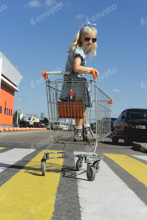 Preview: little adorable kid having fun in shopping cart at parking