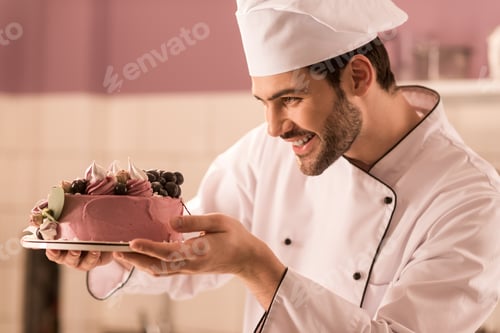 Preview: side view of smiling confectioner looking at cake in hands in restaurant kitchen