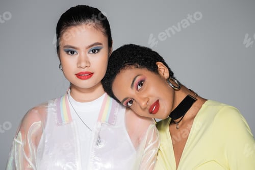 Preview: Stylish african american woman with red lips looking at camera near asian girlfriend isolated on
