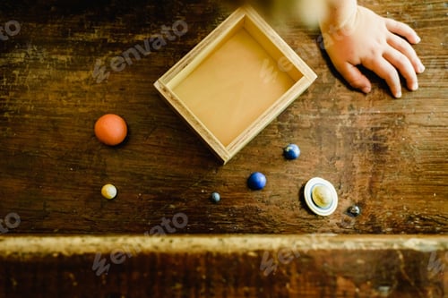 Preview: Child playing with small toy planets on an old wooden table.