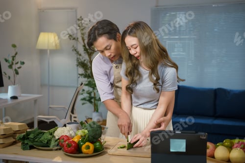 Preview: Asian couple cooking healthy food following online recipe on tablet in kitchen