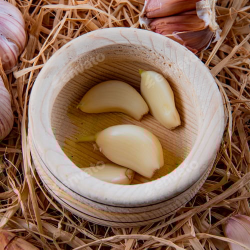 Preview: close-up view of peeled garlic cloves in garlic crusher on straw background
