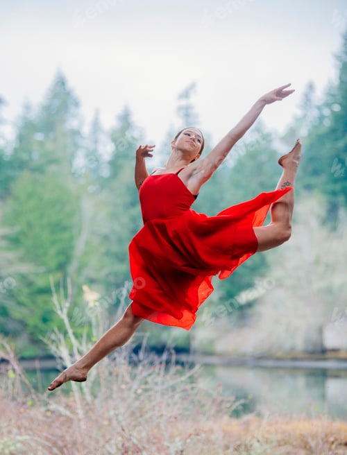 Preview: Dancer in a flowing red dress gracefully leaps in a forest setting. USA
