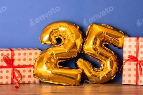 Preview: golden foil balloon numbers party decor on wooden table against blue wall.