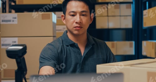 Preview: Close-up Asian man use barcode machine scan data in box and register online order detail in laptop.