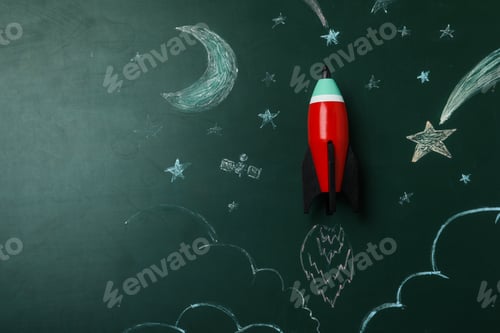 Preview: Bright toy rocket and drawings on chalkboard, top view. Space for text