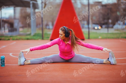 Preview: young woman stretching legs on sports court outdoors