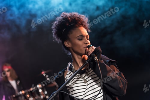 Preview: Female singer with microphone and rock and roll band performing hard rock music on stage