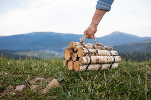 Preview: Man traveler hands holding firewood for fire in mountains. place for inscription.