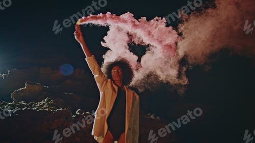 Preview: Activist waving colorful bomb at night outdoors. Confident woman under smoke