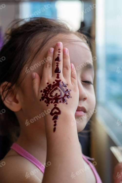 Preview: Portrait of Henna ornaments on little girl's hand covering face.