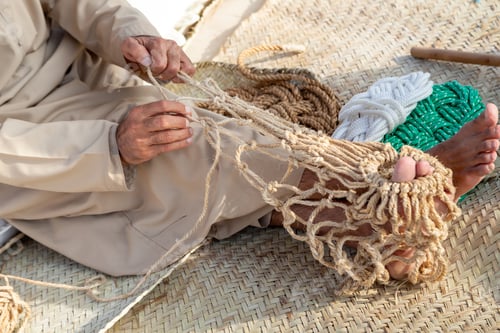 Preview: Old man is knitting traditional fishing net, hands in frame. Cultural heritage of UAE.