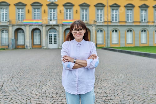 Preview: Middle-aged female teacher posing against background of educational building