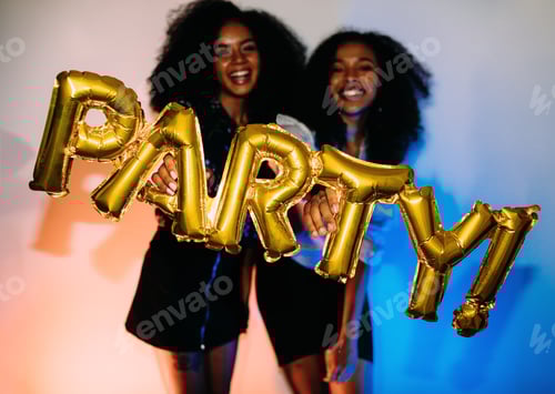 Preview: Happy women holding party balloon, standing indoors near a wall