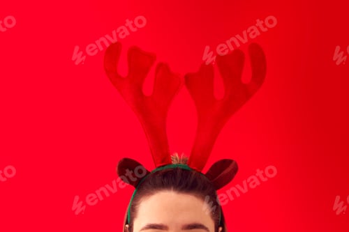 Preview: Close Up Studio Shot Of Woman Wearing Christmas Reindeer Antlers Headband Against Red Background