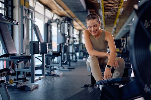 Preview: Happy female athlete exercising on rowing machine at health club.
