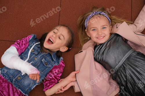 Preview: Girl supports her cheerful laughing friend with broken arm and a cast on forearm